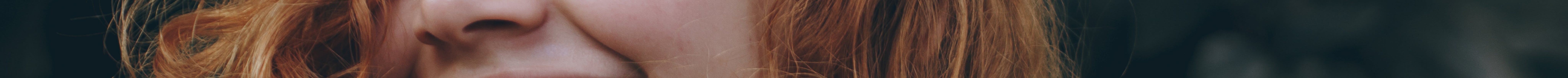 A candid portrait of a joyful woman with curly red hair, expressing natural beauty and happiness.