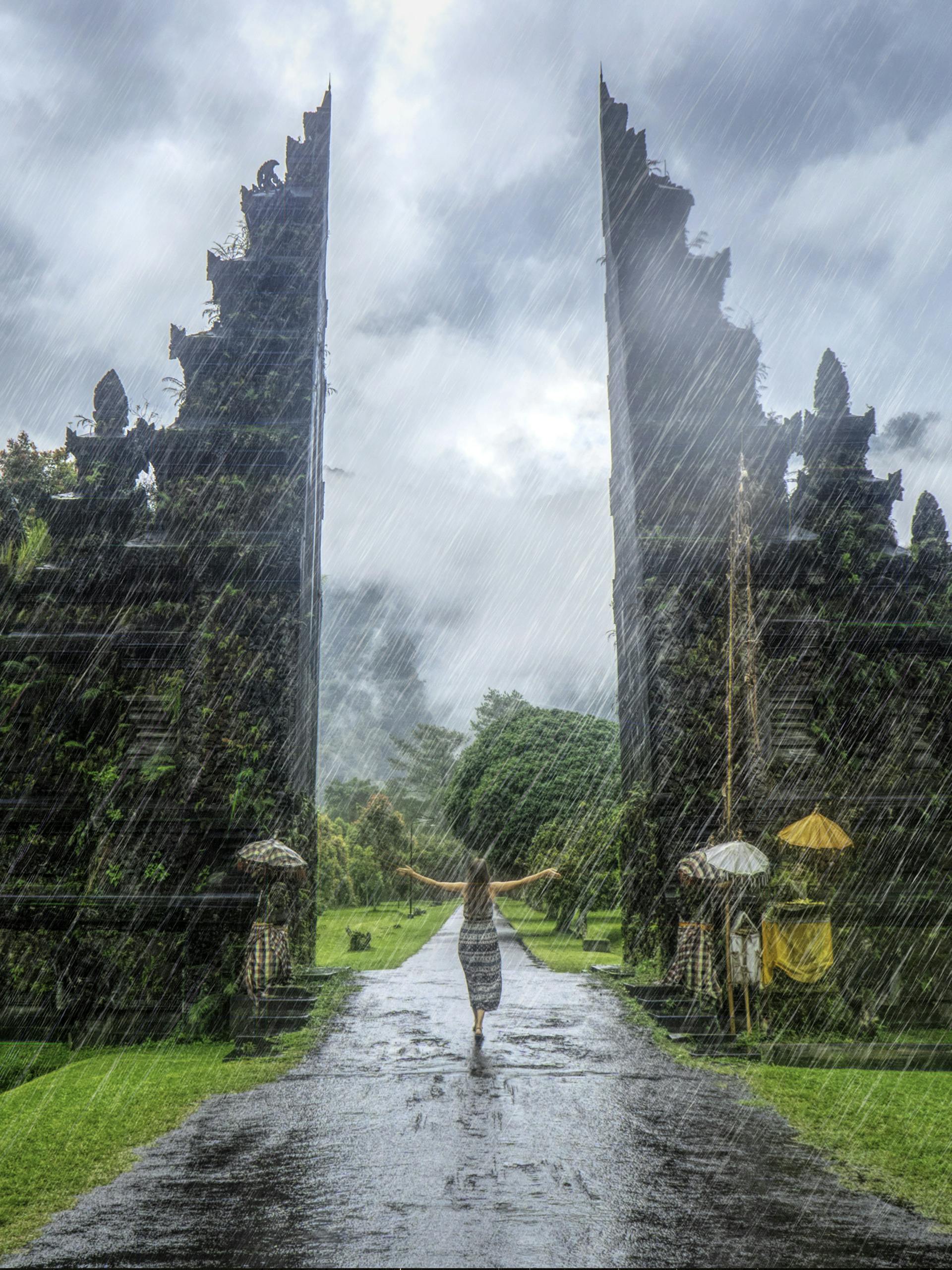 Woman in vibrant rain at iconic Handara Gate, Bali. A magical travel moment.