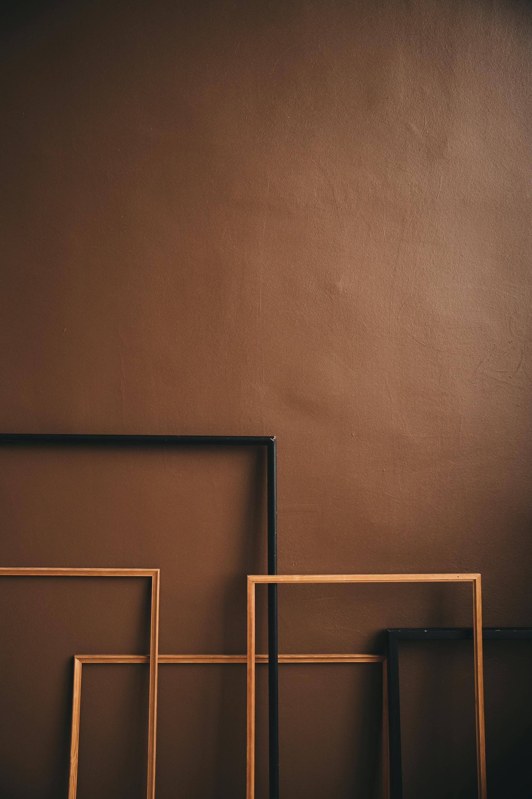 Artistic arrangement of empty wooden frames against a brown wall, showcasing minimalist design.