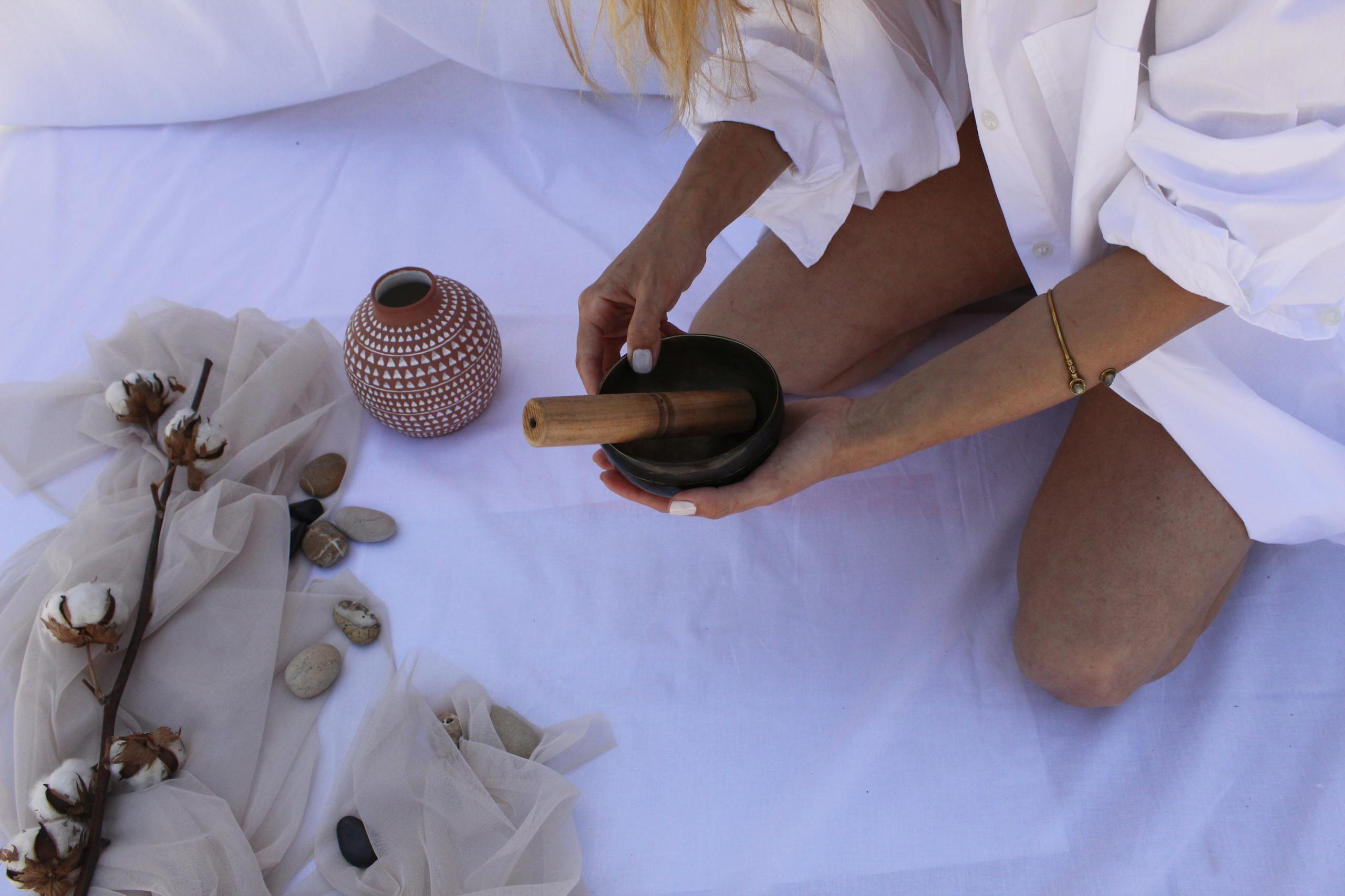 A close-up view of a woman using a mortar and pestle on white fabric, surrounded by natural elements.