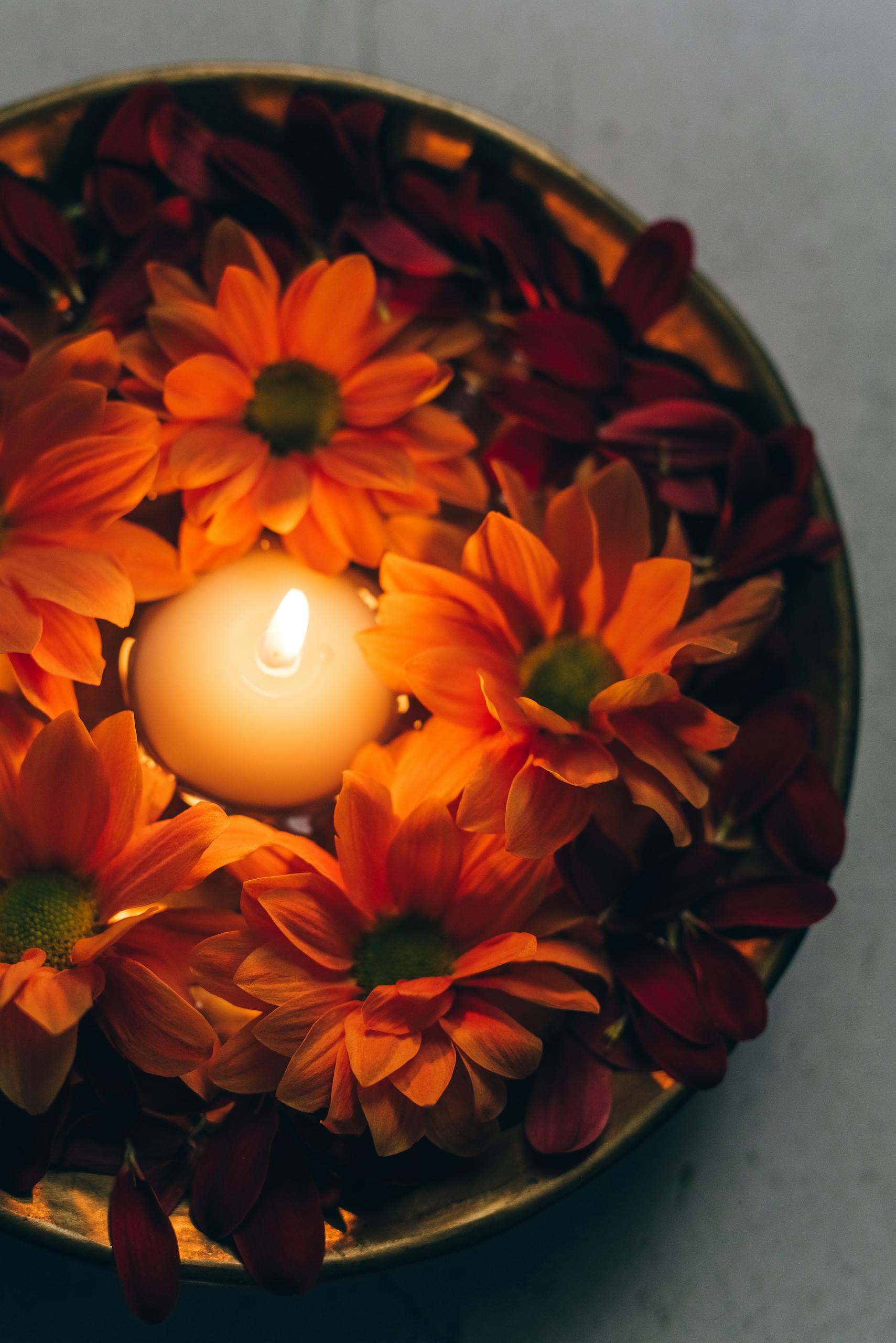 Close-up of a lit tealight surrounded by vibrant flowers in a bowl, perfect for festive decor.
