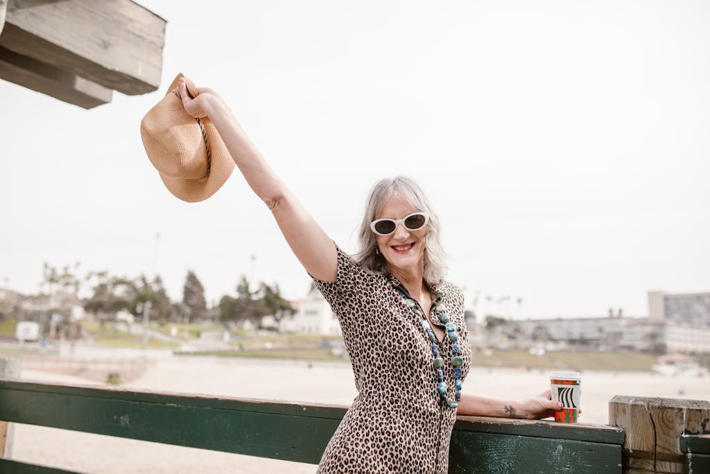Stylish senior woman with hat at the beach, embracing life joyfully.