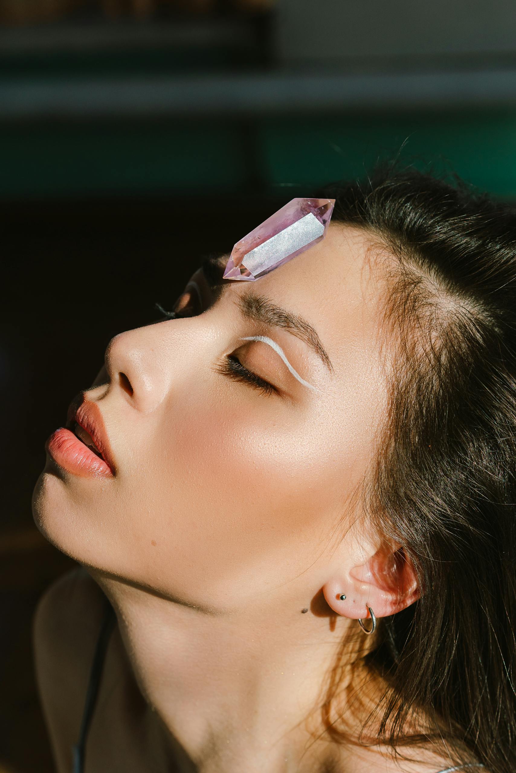 Close-up of a woman with a crystal and artistic eye makeup in sunlight.