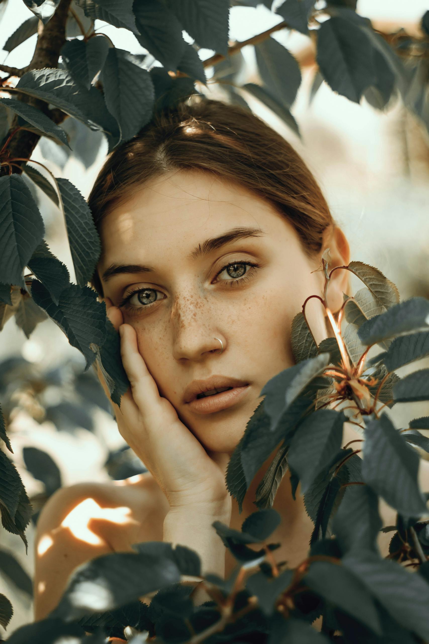 Portrait of a freckled woman surrounded by leaves, evoking natural beauty and serenity.