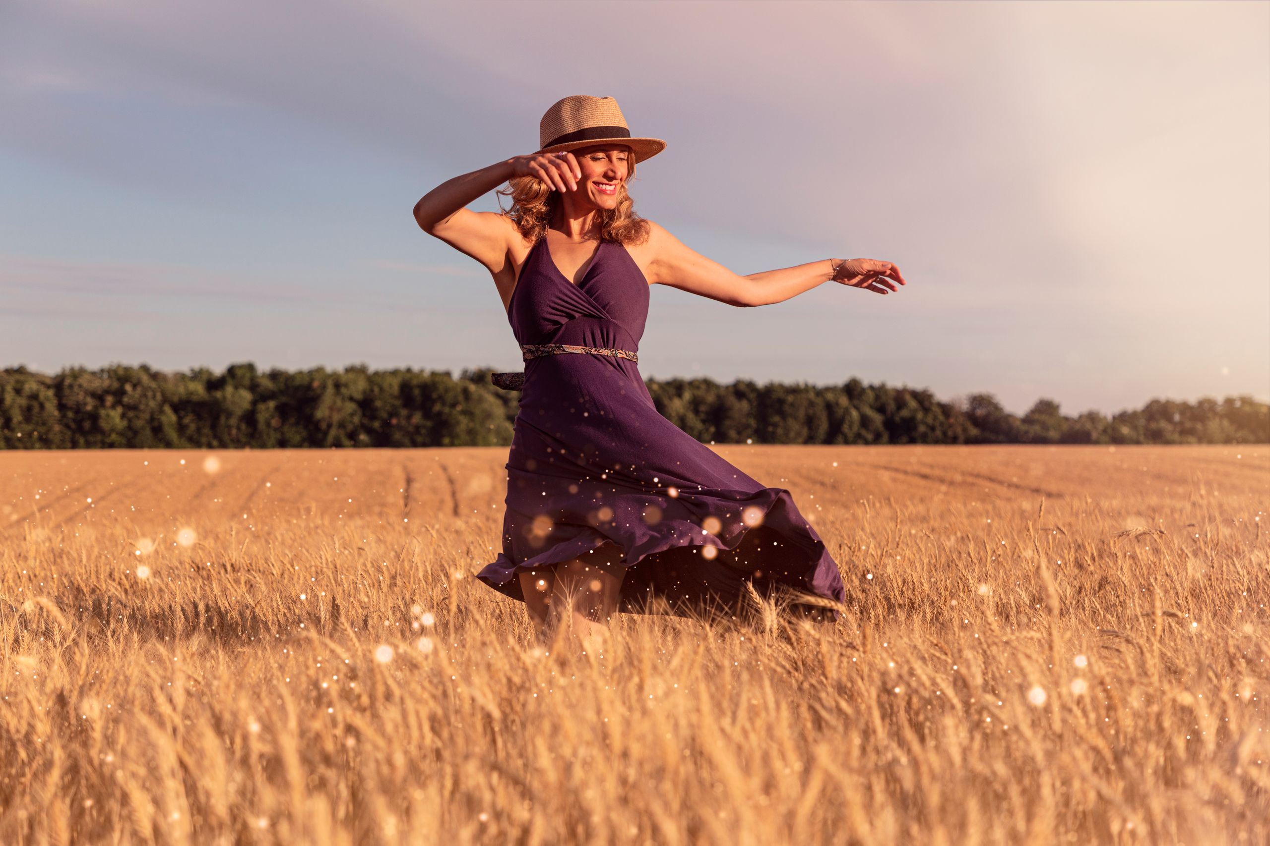 Woman in a hat dancing in a sunlit wheat field, capturing the essence of freedom and happiness.